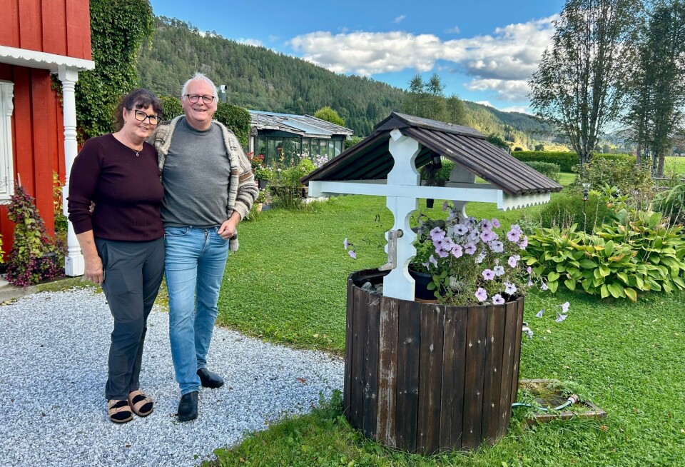 Elin og Ola Helgetun ønsker velkommen inn i hagen på Mo i Øvre Surnadal. Den sjarmerende brønnen skjuler en slangetrommel for enkel vanning i hagen. Ektepar foran en hjemmesnekret brønn med blomster i.