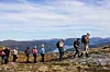 Flere turkledde personer som går på rekke og rad oppe på fjellet. Sommer og lettskyet himmel.