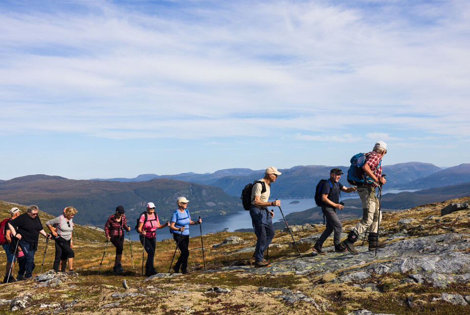 Friskt og lett oppå fjellet. Flere turkledde personer som går på rekke og rad oppe på fjellet. Sommer og lettskyet himmel.