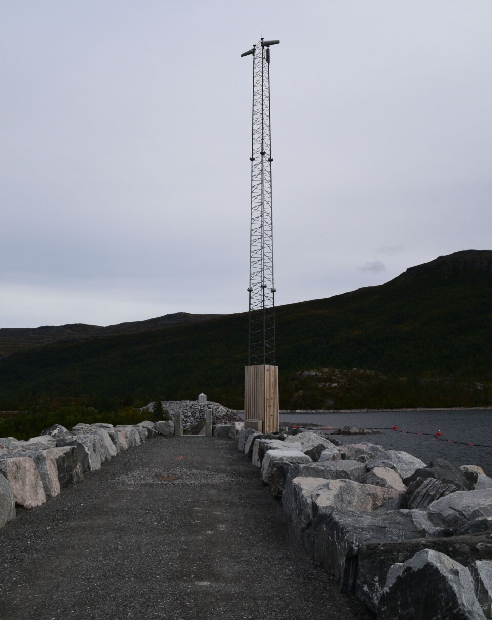 Denne mobilmasta er ny, og har sikret bedre mobildekning i området. Ei mobilmast på toppen av en stor demning på fjellet. Sommer og blå himmel.