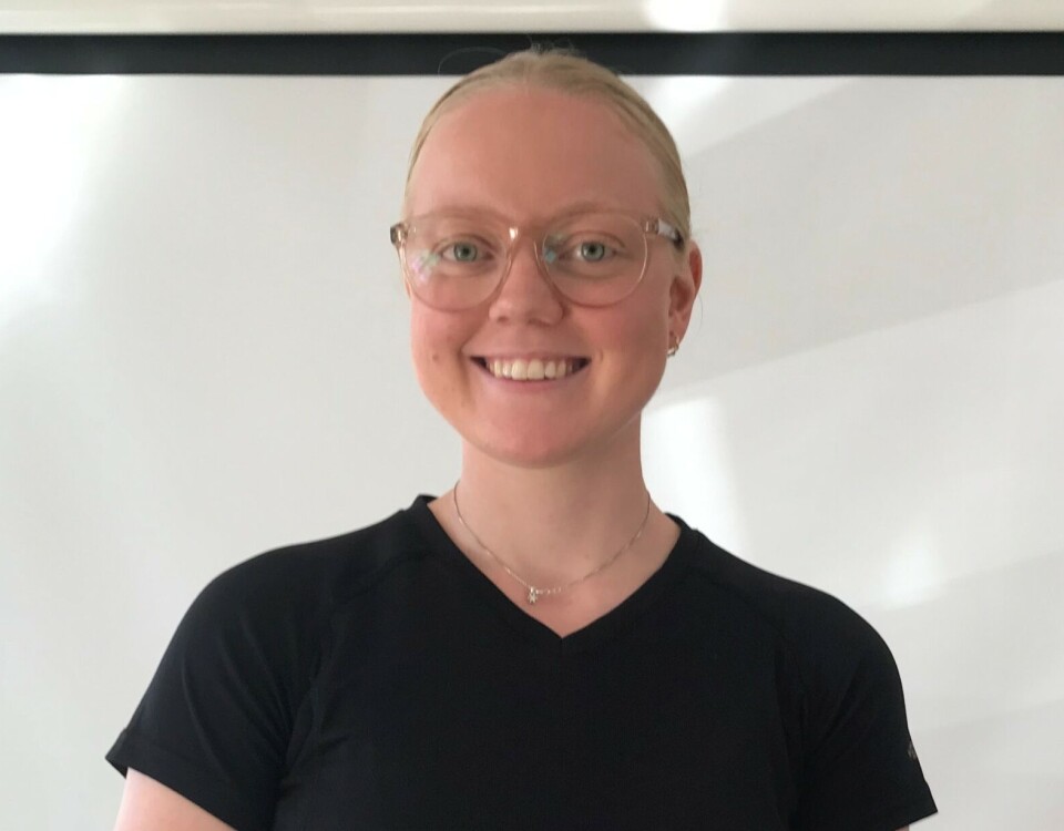 Margit Nikoline Langballe er ny instruktør i 'Sterk og stødig' Jente med glatt lyst hår og briller med sort t-skjorte står i rom foran et lerret