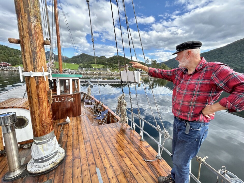 Odd Ragnar Bekken har mange planer for å restaurere den flotte båten. Den store masta står for tur i vinter. Mann i rutete skjorte står og peker på masta om bord i en båt.