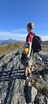Gutt med sekk står på en fjellknaus og ser mot fkell i bakgrunnen.