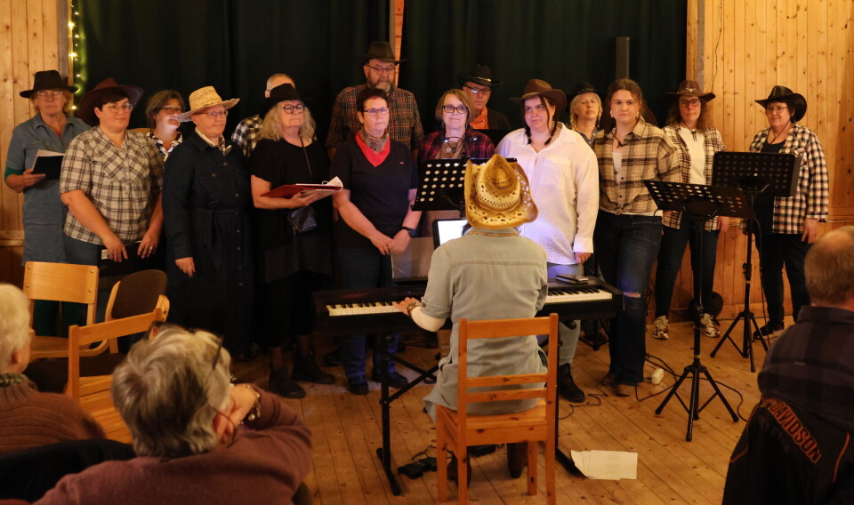'Kor Gøttj' trakk fulle hus på sangkveld i Granheim. Kor med countryantrekk foran scene. Dirigent sitter foran ved pianoet.