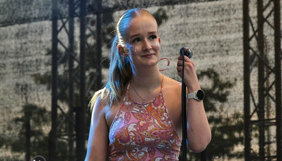 Ida Mo er klar for årets 'Merry Fu**ing Christmas 2025' Bildet viser en ung kvinne med hestehale stående på en scene, pg hun holder i en mikrofon på et mikrofonstativ.