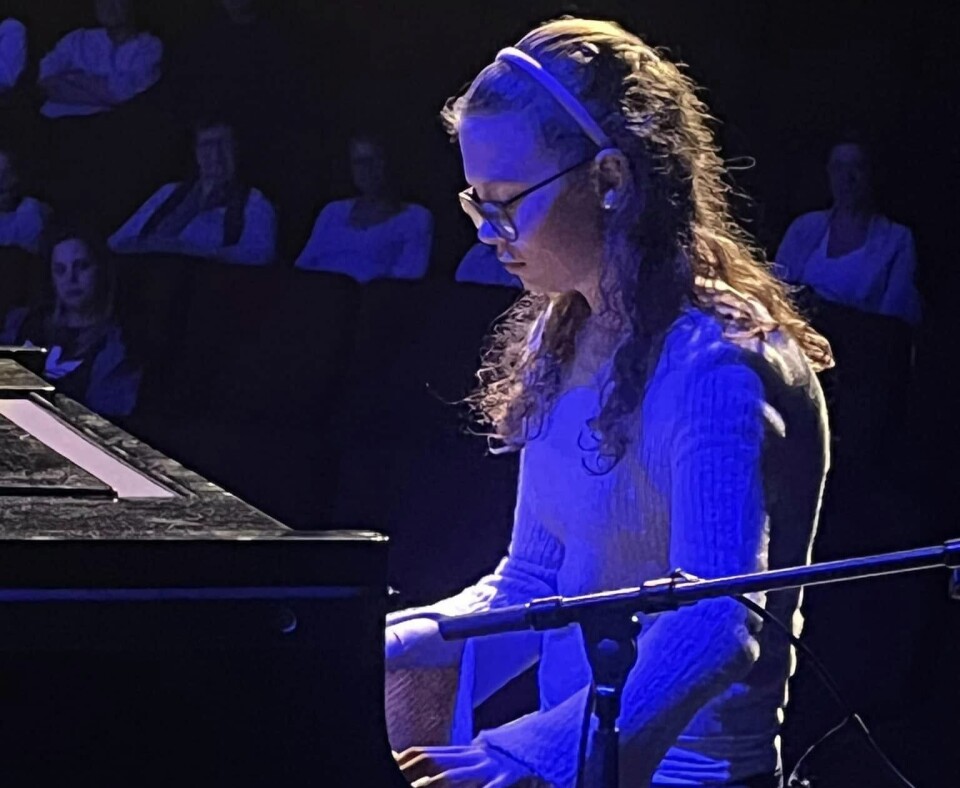 Magni på piano. Bildet viser en ung jente foran et piano på en scene. Hun ser konsentrert ned mot tangentene, hun har et blått scenelys på seg, og vi ser publikumet sittende i et mørkt amfi bak henne.