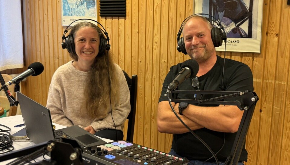 Fjorårets Farmen-deltaker Svein Håvard Saksen sammen med podkastvert Gunn Elin Røen. En dame og en mann sitter og smiler med øretelefoner og har mikrofoner foran seg som er festet på bordet. En bærbar-PC, et miksebord og mange ledninger på bordet.