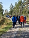 Ei stor gruppen turkledde folk som går på en skogsvei. Høstvær og blå himmel.