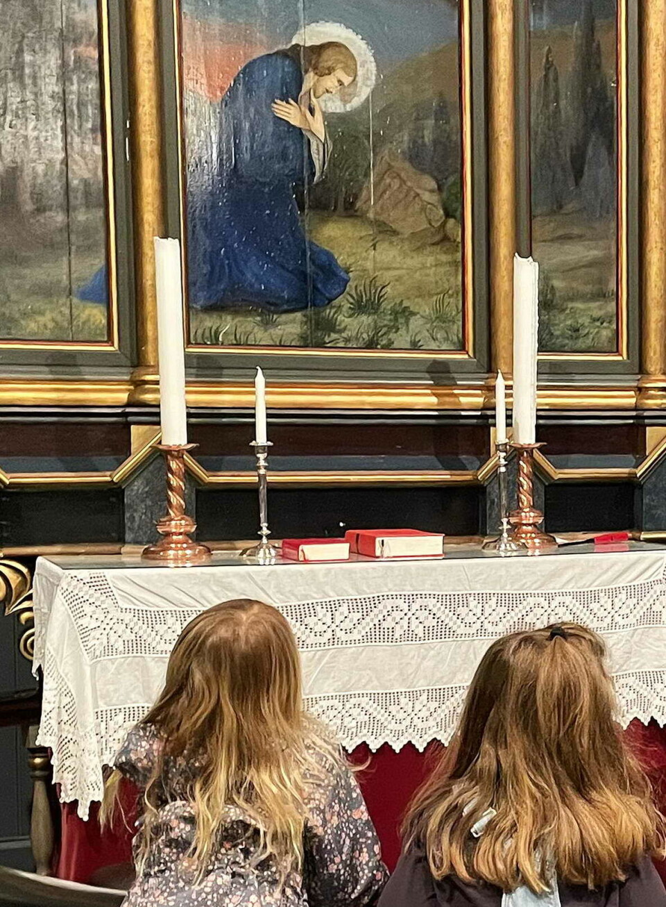 I programmet blir dei yngste kjent med altartavla og andre vakre deler av kyrkja si. To små jenter som ser opp på altertavla i kirka.