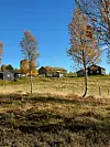 Et setertun med flere bygninger på fjellet. Høstfarger, sol og skyfri himmel.