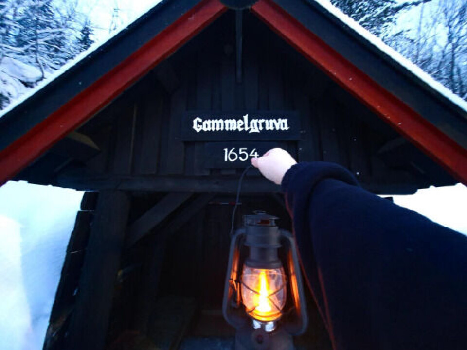 Gammelgruva. Ei hand som holder fram ei gammeldags parafinlampe, foran en gammel gruveinngang.