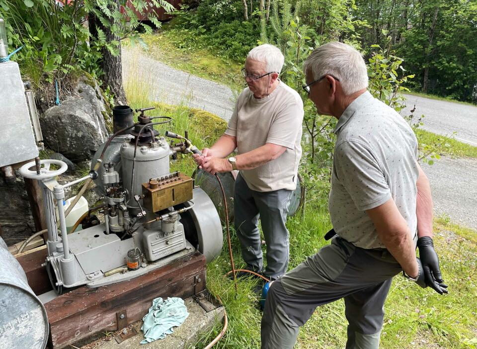Mange rosa innsatsen til Sabb-maskinistane Peder Sæther (med fyrlampa) og Anders Vaagland. To menn med grptt hår som titter på en stor gammel motor, utendørs på grønt gress.
