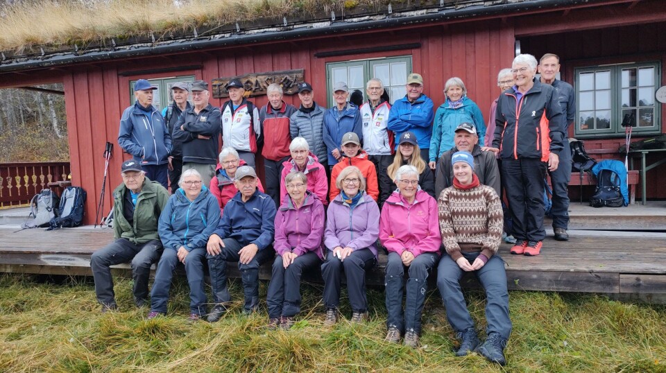 Sesongens siste tirsdagstur gikk til Gammelseterøyan Ei stort gruppe med turkledde folk oppstilt for fotografering foran ei hytte med torvtak.