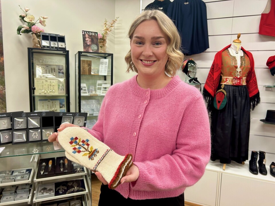 Kirsten Næss ved Husfliden i Surnadal viser frem en brudevott fra Sunndal. - Det er bare å stikke innom for inspirasjon, så skal vi hjelpe, lover hun. Dame med rosa strikkegenser og en pen hvit vott med broderier.