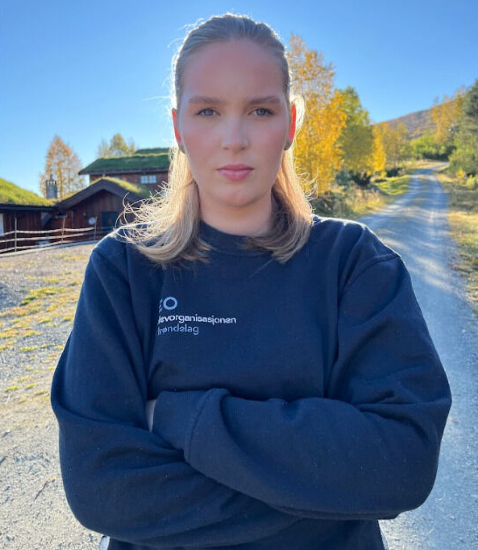 Carina Romundstad, leder i Elevorganisasjonen i Trøndelag. Portrettbilde av ei ung dame med streng mine og hendene foldet foran brystet. Hus og en vei og blå himmel i bakgrunnen.