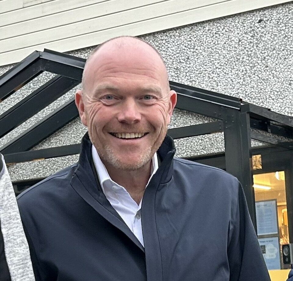 Lars Ove Valaas-Breivik Smilende mann med lite hår står utenfor et bygg, Blå ytterjakke og lyseblå skjorte.