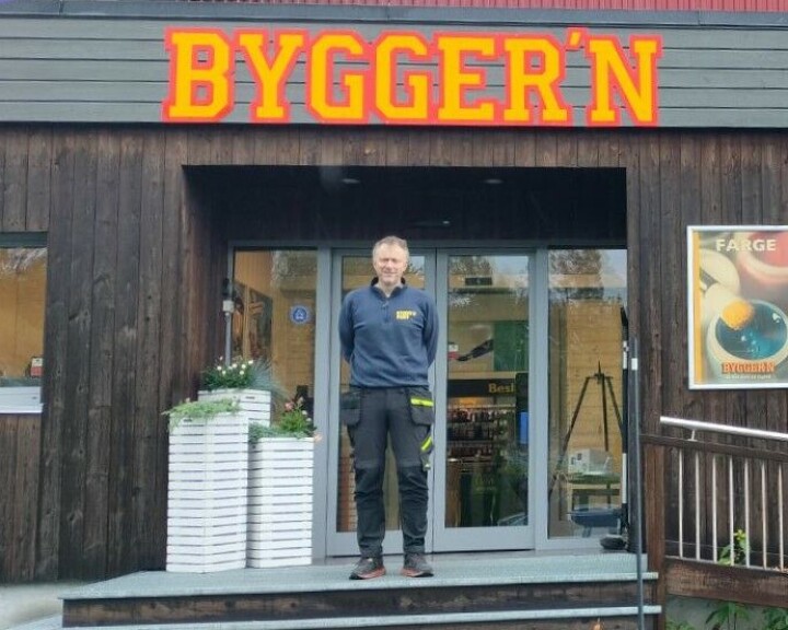 Her står Ingebrigt Løfald på trappen til Bygger`n Rindal. Her står en mann ved inngangen til et hus, ved inngangen er det en trapp og noen blomsterkasser.