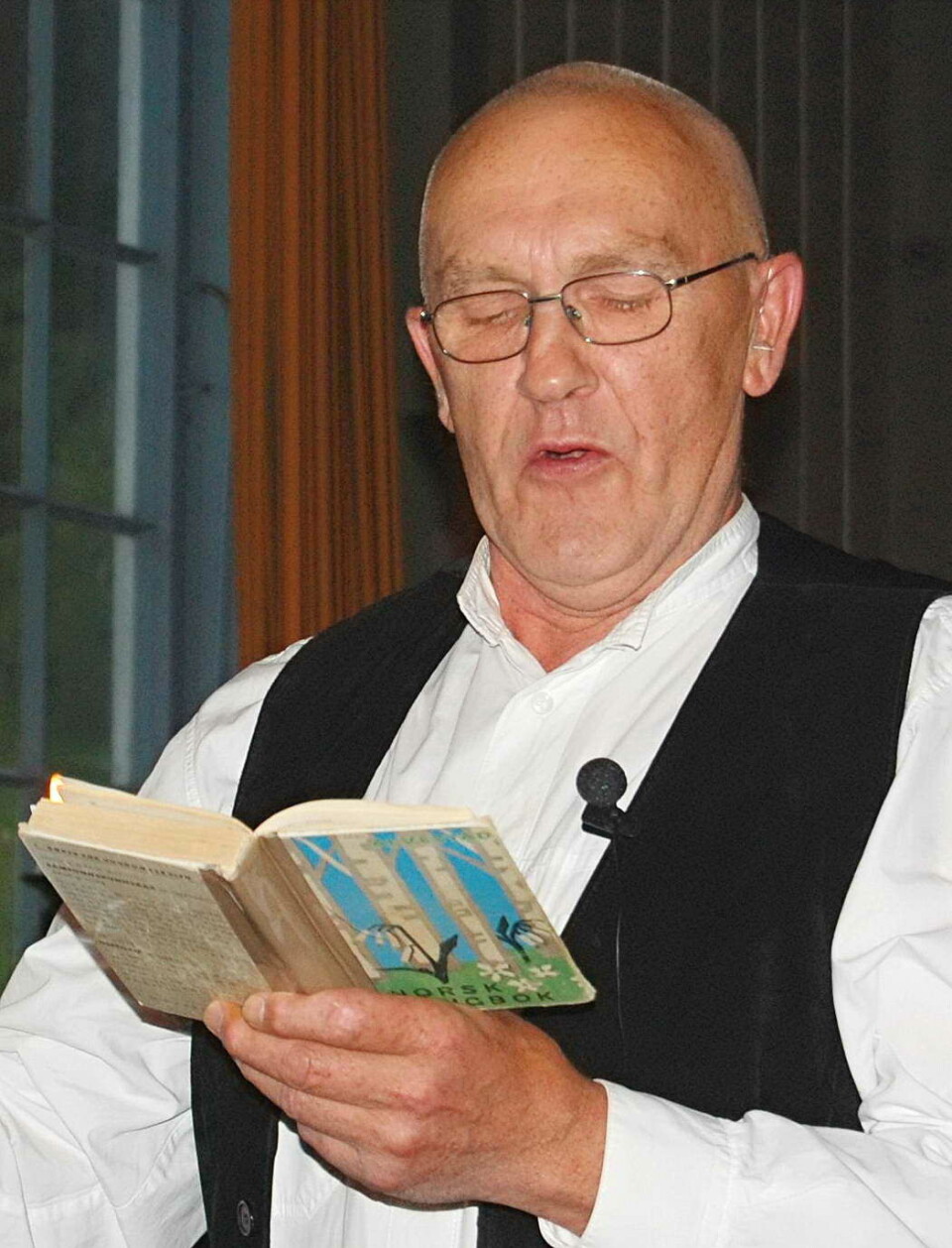 Torgrim Tunes vil deklamere gode vers. En mann med briller og lite hår, som står og leser fra ei gammel bok.