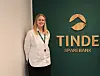 Dame i hvit skjorte ved et skilt med Tinde Sparebank logo