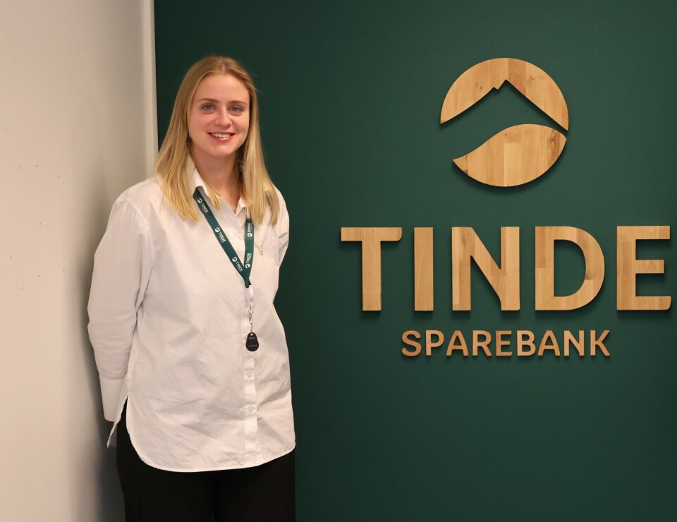 – Å jobbe i bank er en fin og trygg arbeidsplass, med mange muligheter i fremtiden, sier Brit Ragnhild Bergheim. Dame i hvit skjorte ved et skilt med Tinde Sparebank logo