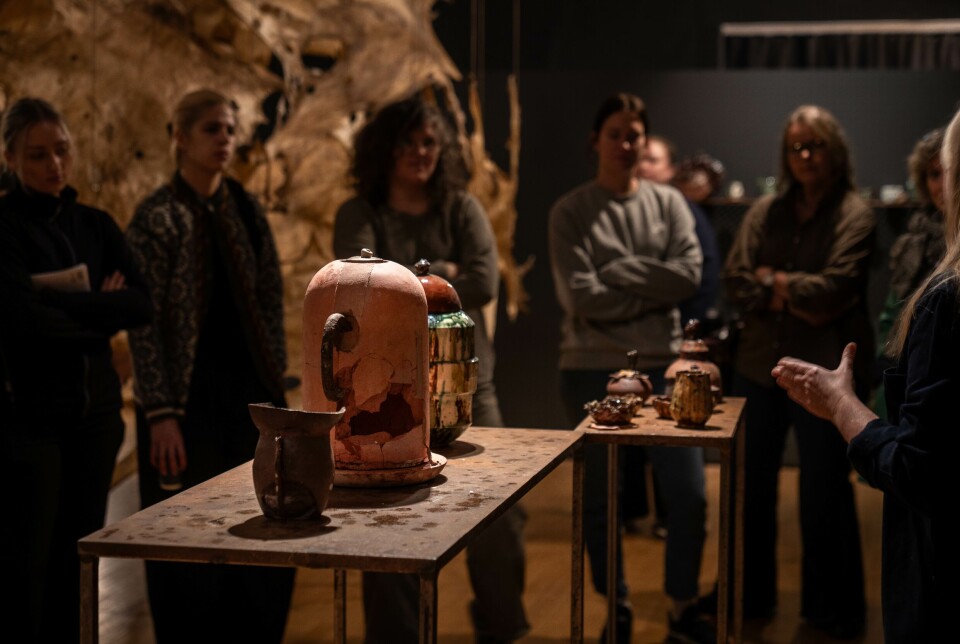 Frå omvising i utstillinga Doggerland ved Møre og Romsdal Kunstsenter. Utstillinga står til 1. november. Flere personer s0om står og ser på ulike gjenstander på et bord på en kunstutstilling.