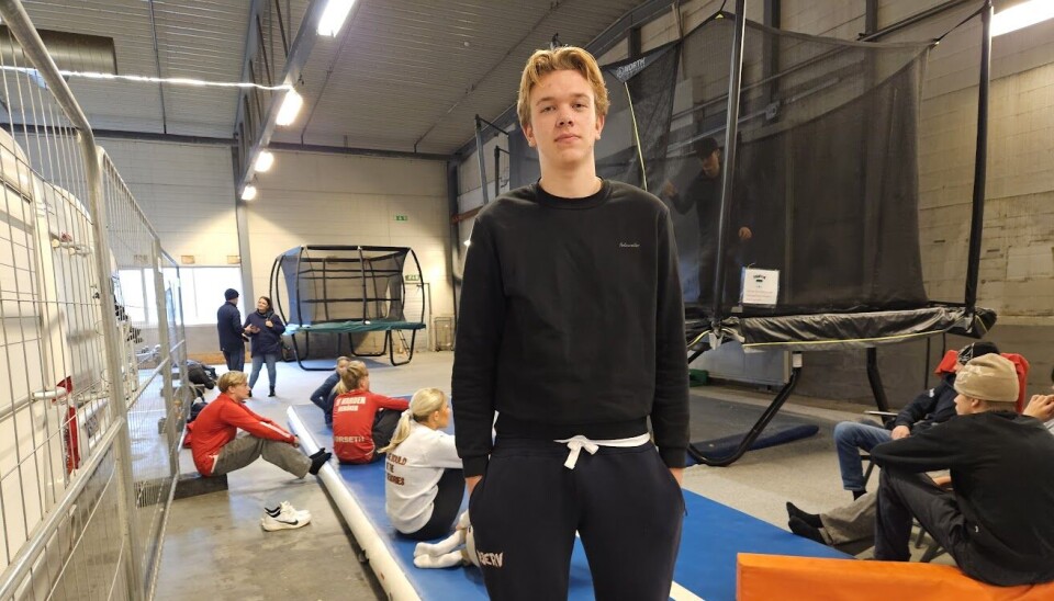 Lars Vaseng Kvammen fra Surnadal er trener for freeskigruppa i Surnadal IL. Bildet viser en ung mann stående i et stort lagerbygg. Bak han ser vi en lang turnmatte på gulvet, og en trampoline med nett.