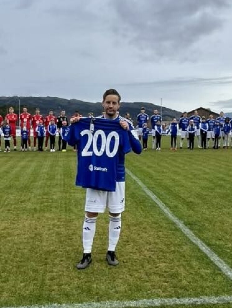 Håkon Bredesen med skjorta som markerer sine 200 spilte kamper for Surnadal IL. fotballspiller holder opp blå skjorte med 200 på