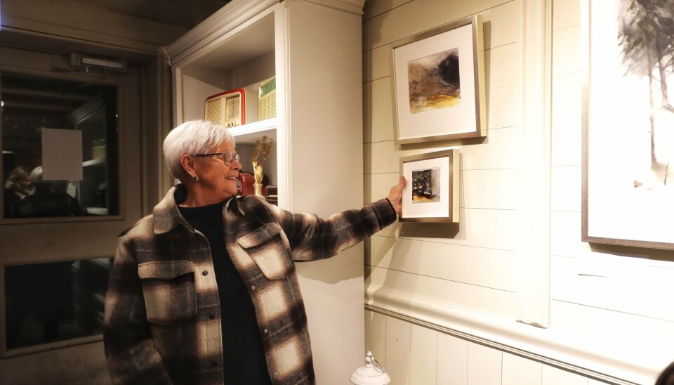 Eli vurderer å kjøpe begge bildene. Hvithåret dame i rutete ytterjakke holder ett bilde opp mot ett annet som henger på veggen for å se om de passer sammen.