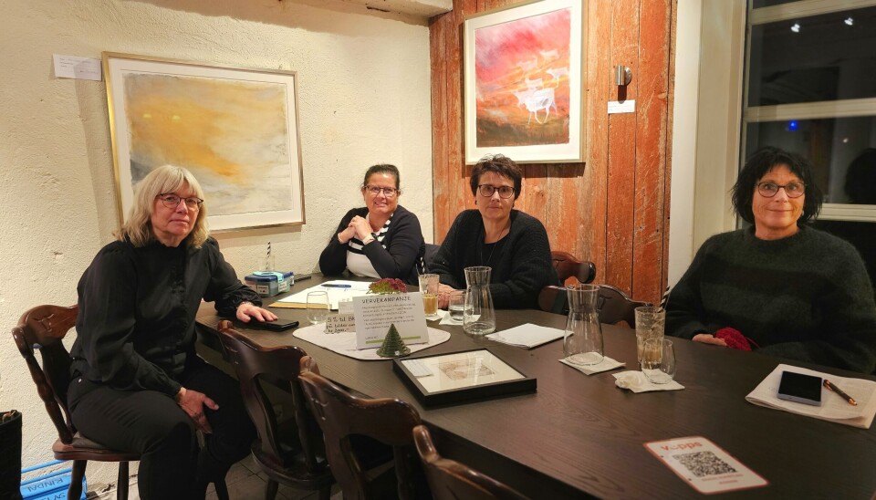 Styret i Rindal kunstlag ved leder Mie Sandø, Anne Norli, Kristin Langli og Anni Karlstrøm 4 voksne damer sitter ved mørkt spisebord med vannglass og papir på bordet, to bilder på veggene bak dem.