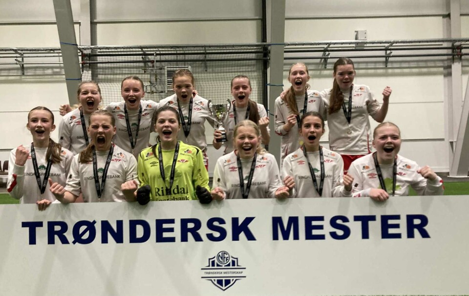 Rindal IL J13 slo Vuku/Stiklestad/Leksdal og ble Trønderske mestere Jenter i hvite drakter som står bak et skilt med 'Trøndersk mester og jubler'