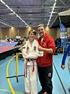 En smilende Taekwon-Do-utøver, en ung gutt, og en voksen gråhåret trener, oppstilt for fotografering.