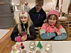 Tre barn som sitter ved et bord, med selvlaget julepynt foran seg på bordet.