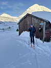 Ei dame på ski foran et seterhus på fjellet. Landskapet er dekket av snø.