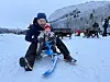 En mann og et lite barn som sitter på et akebrett i snøen.