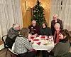 To menn og fem damer rundt et bord med juletre i bakgrunnen