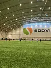 Spillere trener fotball på innendørs kunstgressbane foran stor SODVIN-logo.