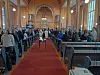 Mennesker står i kirkerader under en seremoni foran alteret.