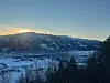 Lav vintersol bak snødekte åser over en dal med snø og mørke trær i forgrunnen.