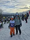 Barn med startnummer 52 og voksen i skiutstyr står i snøen foran alpinrenn.