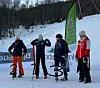 Fire personer med medaljer står på snø foran KIWI-flagg og sponsorbanner i en skibakke.