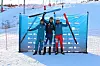 Tre alpinister står foran blå sponsorvegg med ski hevet i et snødekt skianlegg.