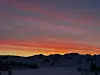 Snødekte åser i silhuett mot rød og oransje vinterhimmel ved solnedgang