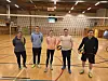 Fem personar står på volleyballbane innandørs med nett og to ballar.