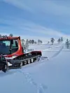 Rød løypemaskin lager skispor i et åpent, snødekt landskap