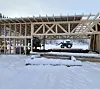 Uferdig trebygg i snø med traktor synlig gjennom den åpne konstruksjonen