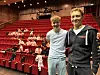 To unge menn foran publikum i stor sal med røde seter.