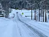 Islagt vintervei gjennom skog med bil og trafikkskilt i bakgrunnen.