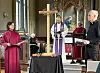 Flere personer leder en seremoni rundt et kors med blomster i en kirke.