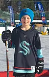 Barn i Seattle Kraken-drakt står med ishockeykølle på utendørs bane.
