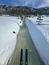 Skispor går langs en frossen bekk mellom dype snøkanter i fjellterreng.